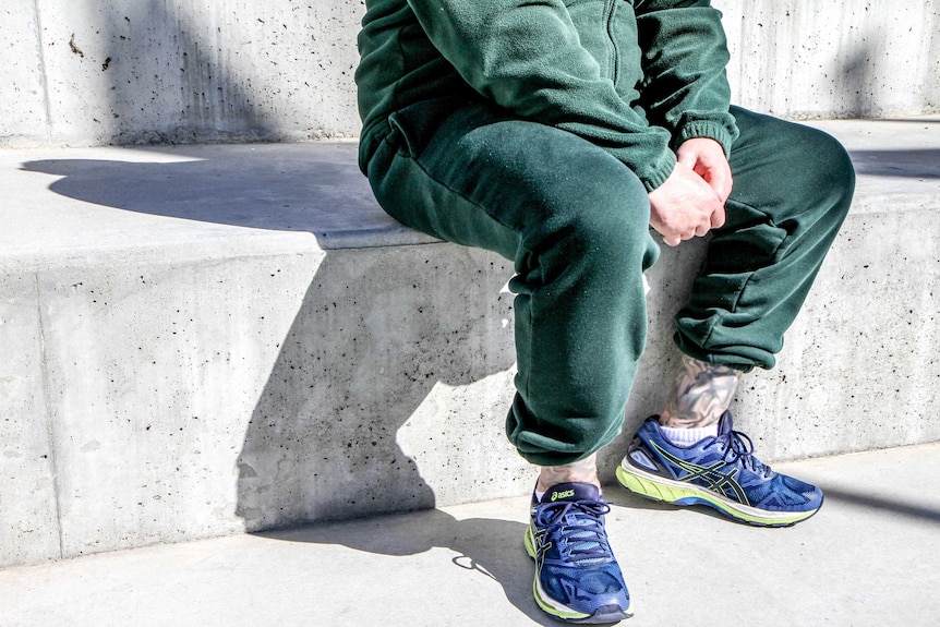 Prisoner sits in green tracksuit.