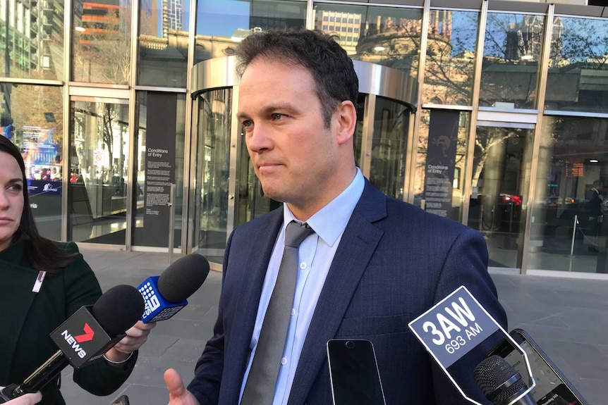 A man in a blue suit speaks to media outside a court.