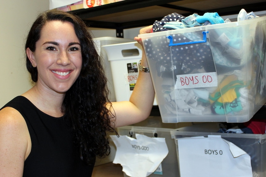 Charity founder takes box of baby clothes from a shelf.