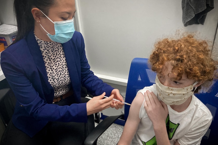 A 12-year-old boy gets vaccinated against COVID-19 by a pharmacists in Sydney.