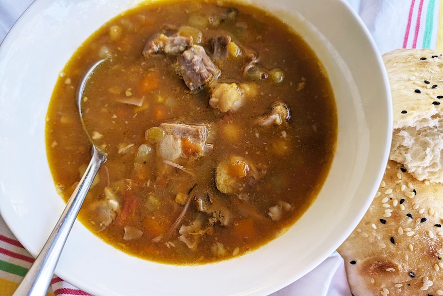 A bowl of brown soup with chunks of lambs and vegetables, and a spoon in it