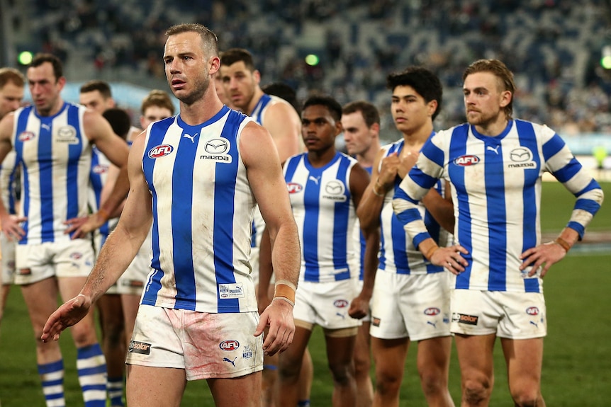 North Melbourne players stand together looking flat after a loss