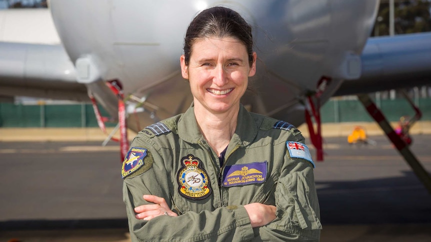 A smiling woman in a flight suit standing in  front of a large plane
