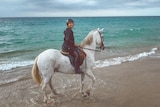 A lady riding a white horse on a beach