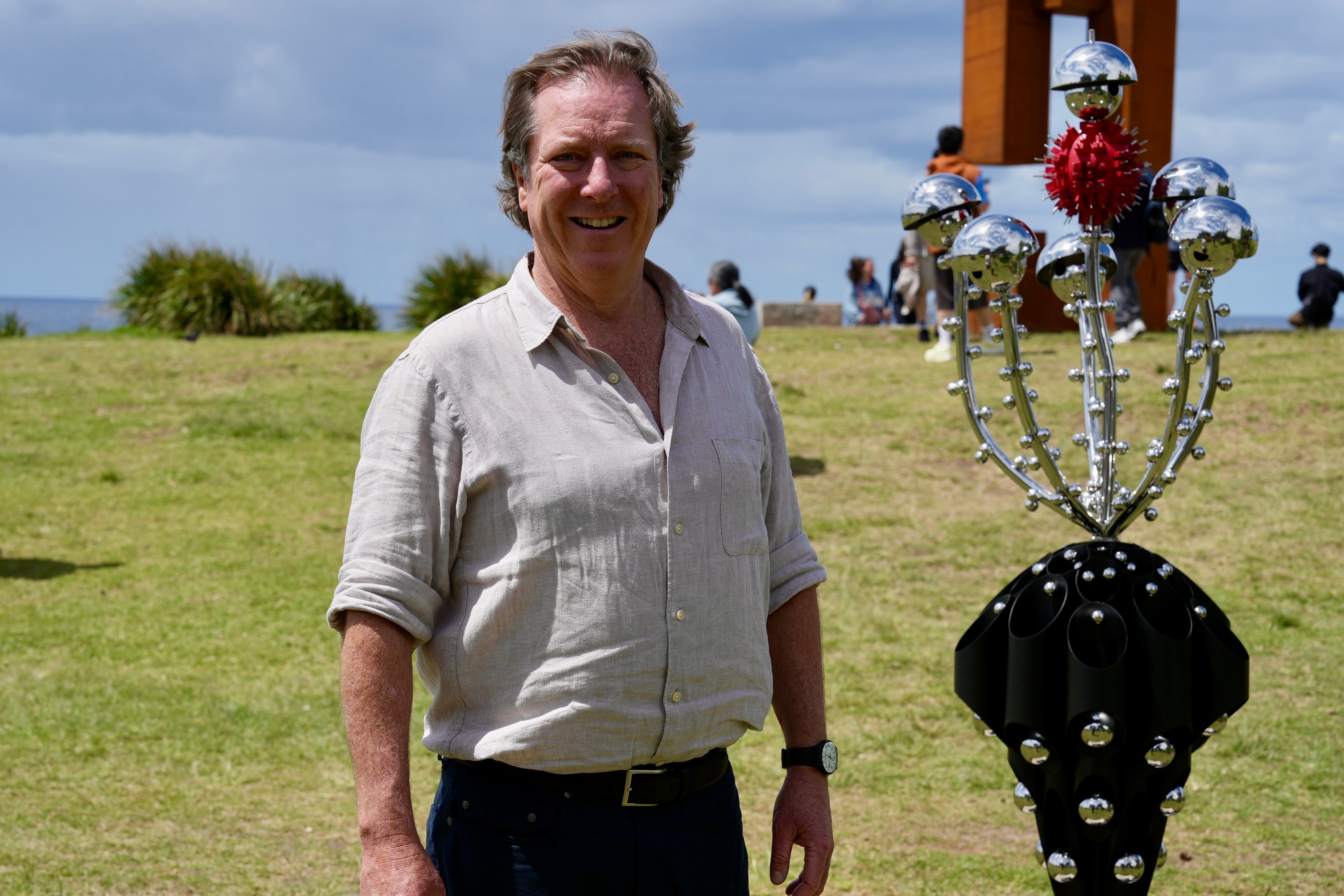 Mr Handley with short wavy brown hair smiles next to five metal reflective balls surrounding a spiky red ball.
