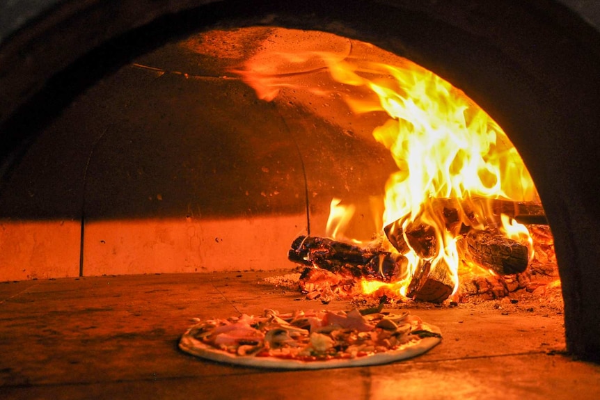 A pizza can be seen being cooked next to fire inside a pizza oven.