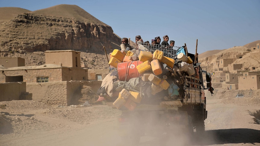 An overloaded truck drives through a village made of mudbricks set against hills.