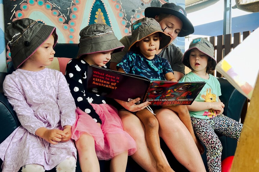 Four young kids at childcare reading a book with a teacher