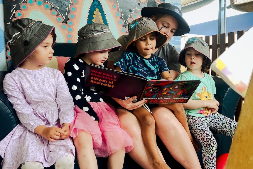 Four young kids at childcare reading a book with a teacher