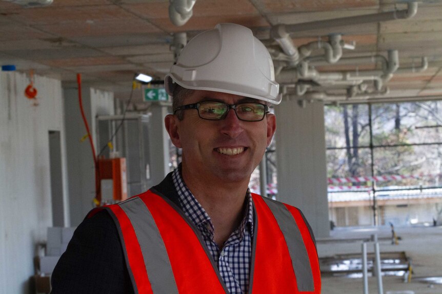 Nicholas Proud, CEO of PowerHousing, in a partially completed home, wearing a high vis orange vest and white hard hat.