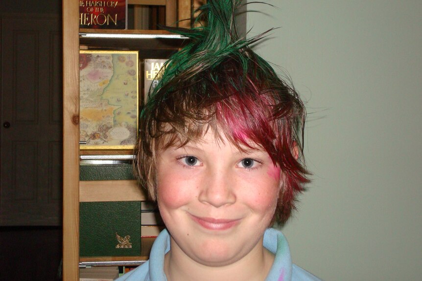 Old photo of Josh Green when he was a child. He has green and red dyed hair and wears a blue school shirt.