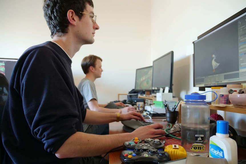 Stuart Gillespie-Cook and Nico Disseldorp work at computers, with gaming consoles on their desks
