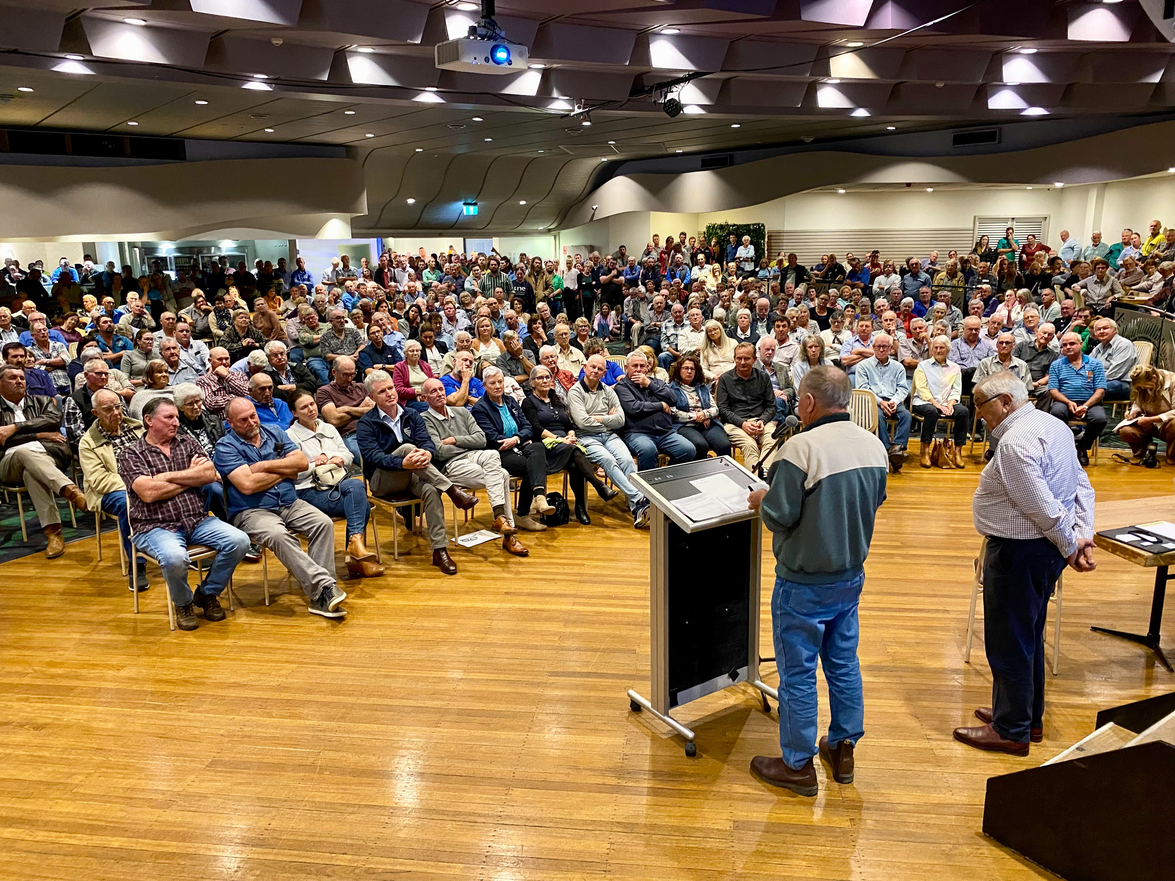 A man standing at a lectern addresses a crowded room.