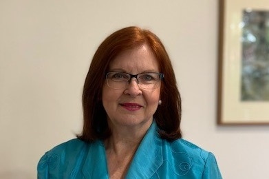 A woman with auburn hair, wearing glasses and a bright blue blazer, smiles at the camera.