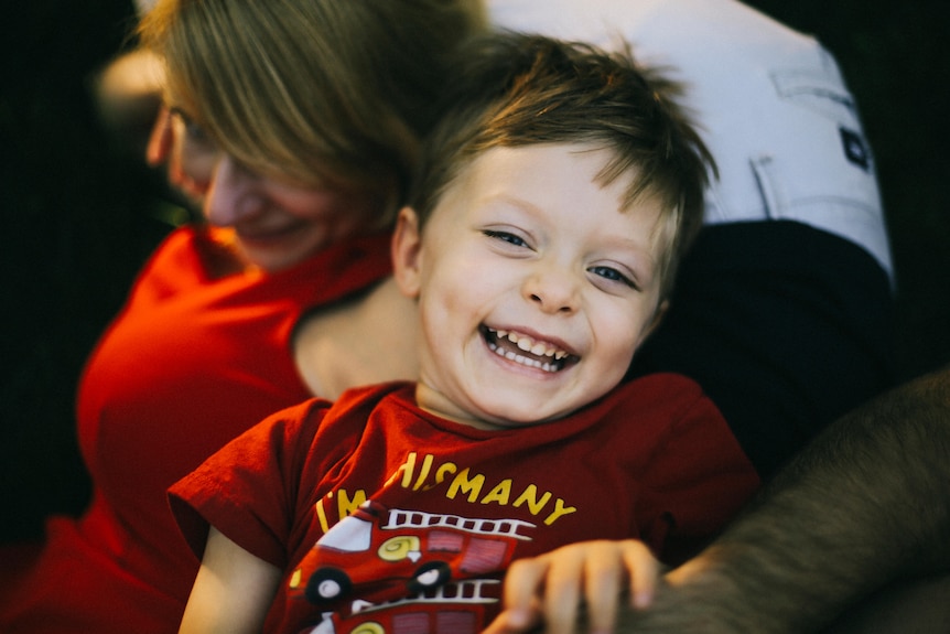 Young boy laughing with mum in background