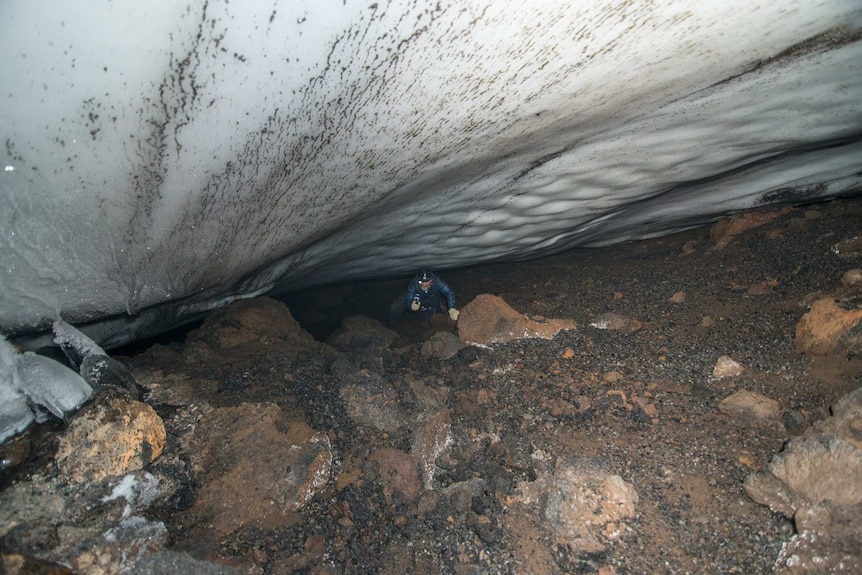 A man looks up holding a light standing at the bottom of an ice cave