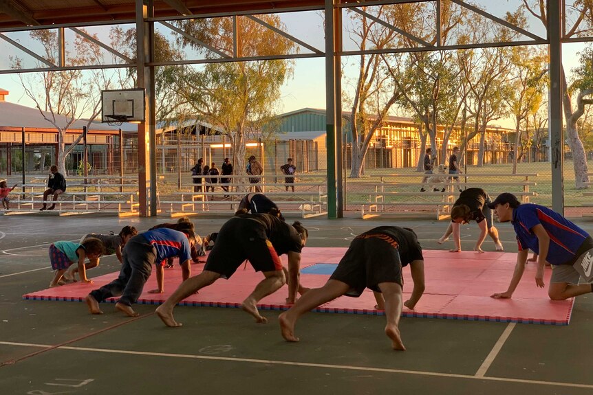 A group of kids stretching on a wrestling mat.