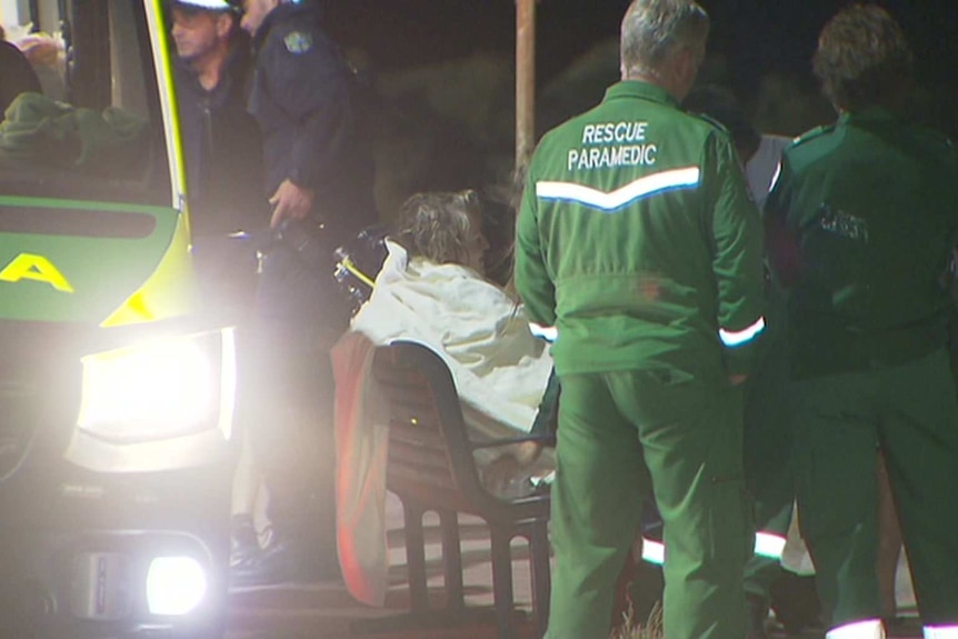 A woman with a blanket on a stretcher next to an ambulance with paramedics