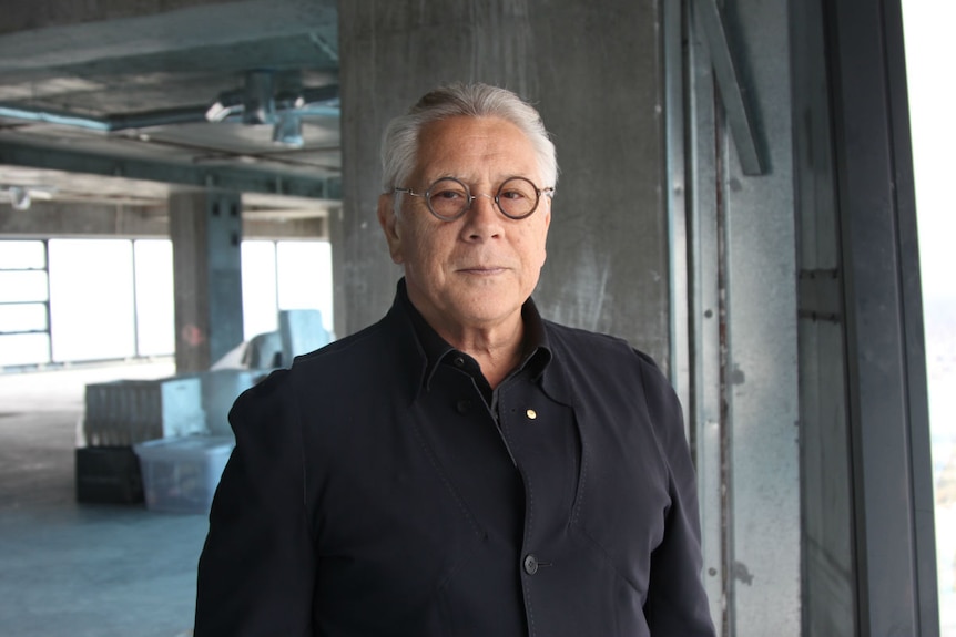 A man stands in a large concrete apartment that has no furnishings or wall coverings yet.