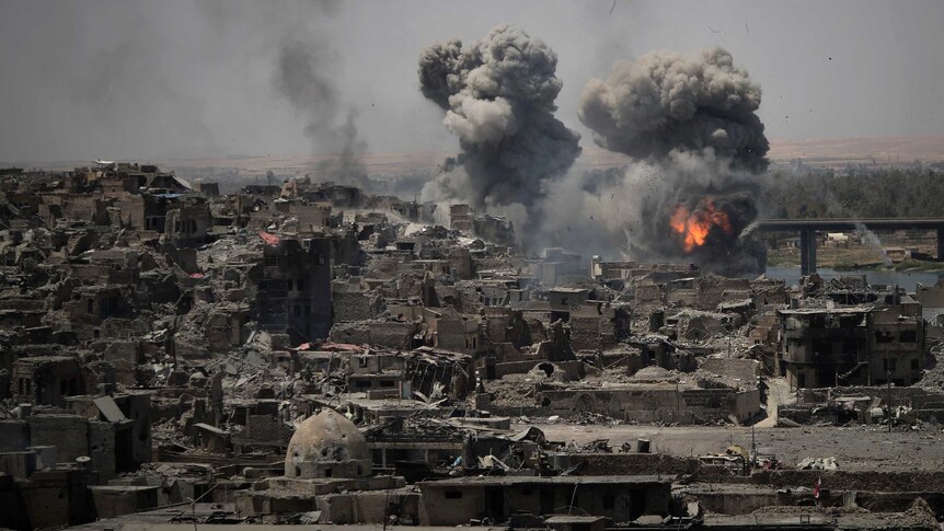 A ghastly image of Mosul in ruins with explosions in the background.