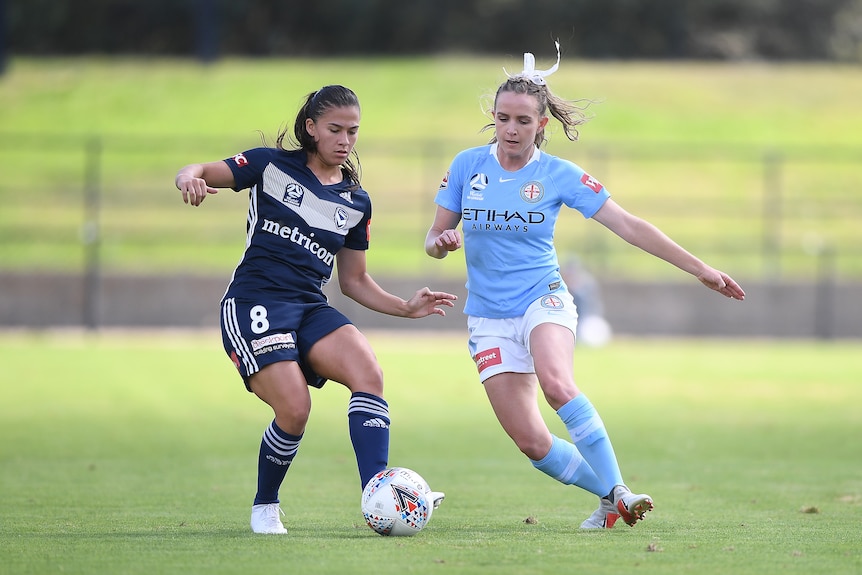 Two female soccer players on the field tussle for the ball