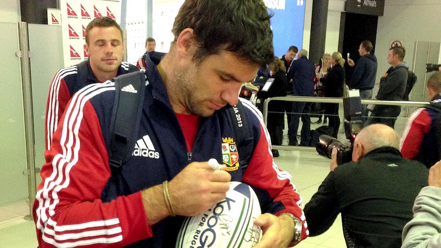 Mike Phillips signs a football at Perth Airport.