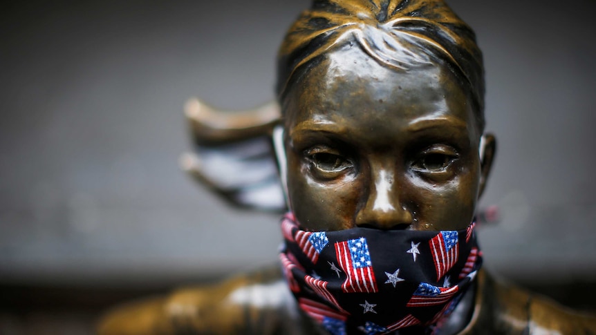 The face of the Fearless Girl statue wearing a face mask with American flags on it.