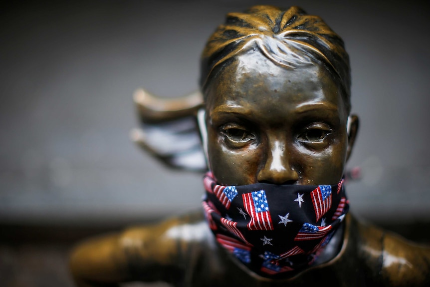 The face of the Fearless Girl statue wearing a face mask with American flags on it.