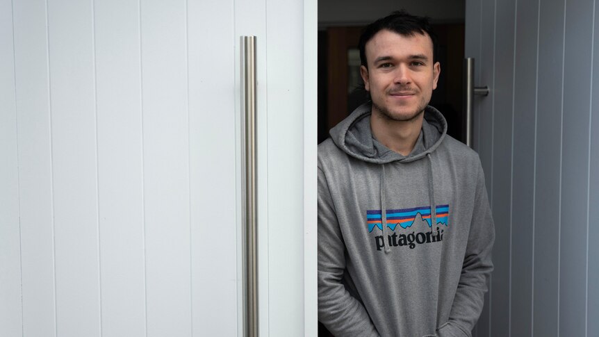A young man in a hoodie stands next to a white door