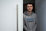 A young man in a hoodie stands next to a white door