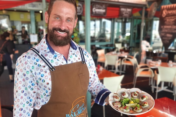 A man in an apron holds a plate of seafood.