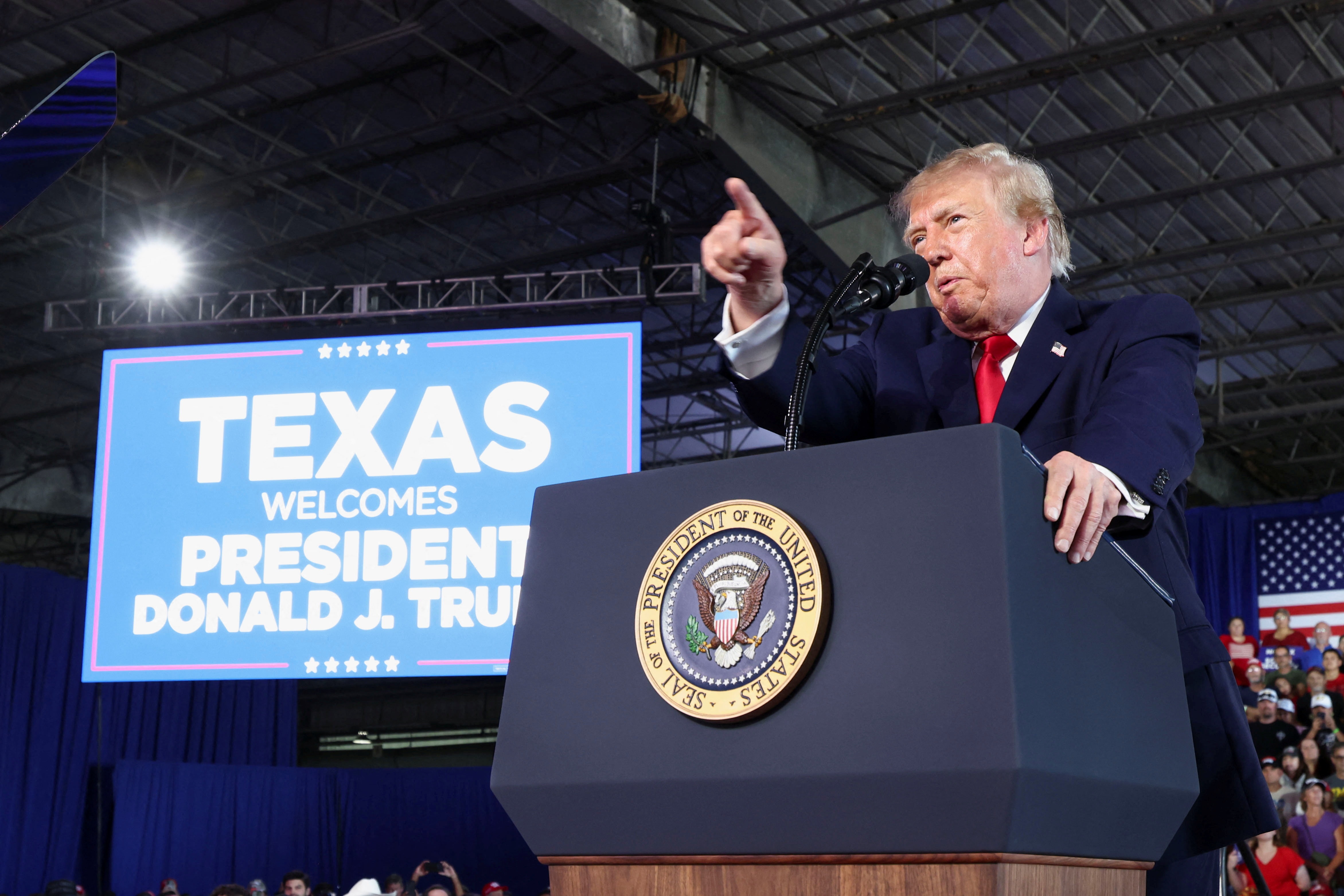 Trump speaks at a podium in front of a sign welcoming him to Texas