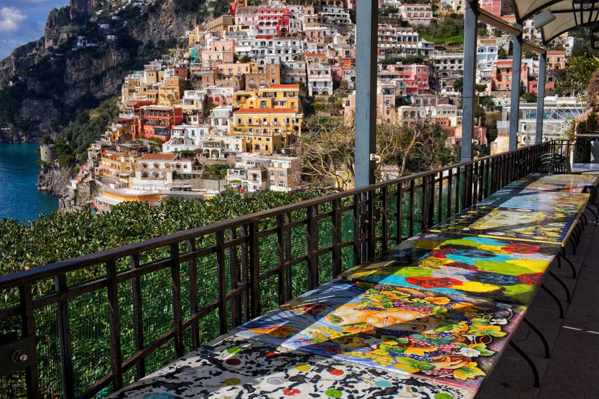 Brightly coloured empty tables on a balcony overlooking the Italian town of Positano