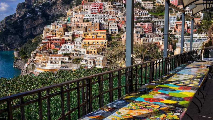 Brightly coloured empty tables on a balcony overlooking the Italian town of Positano