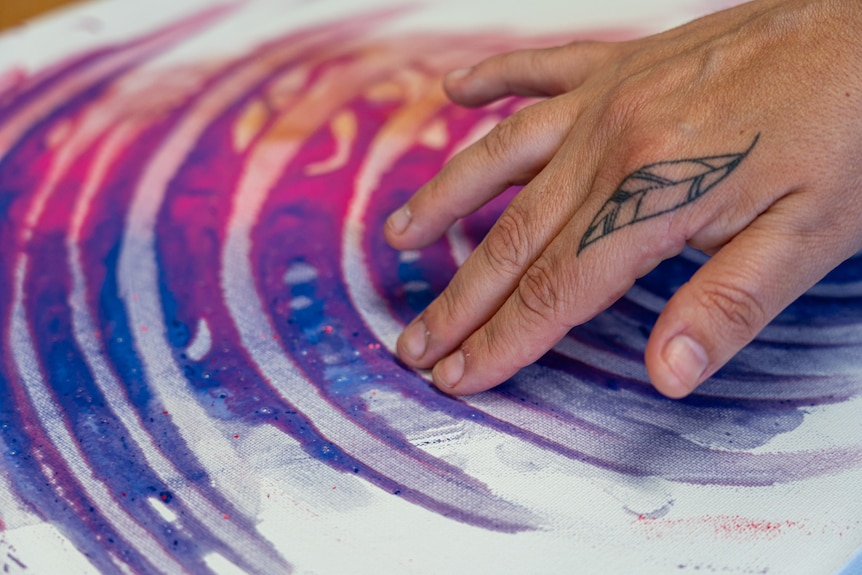 克里用手指在画布上用颜料画出粉色和紫色的半圆。