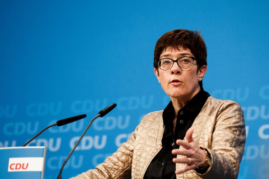 Annegret Kramp-Karrenbauer speaking at a microphone stand.