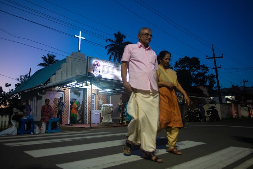 A man and a woman walk across a crossing in the evening.