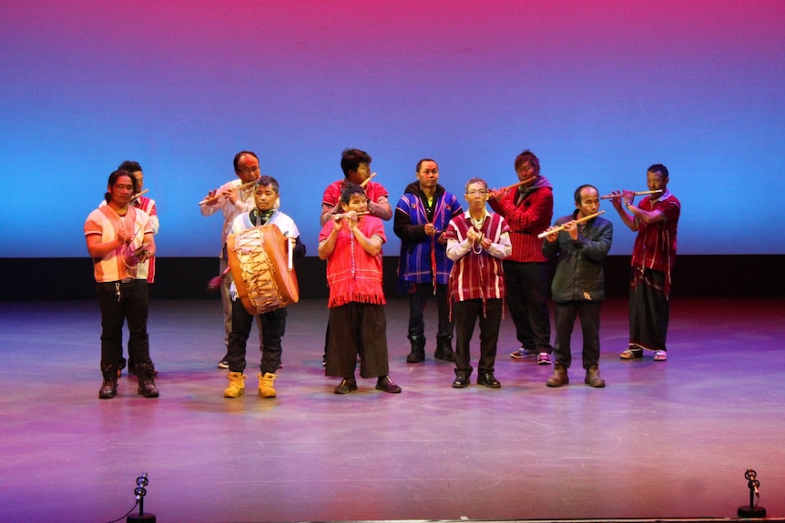 A group of men in colourful clothes stand on a stage playing instruments.