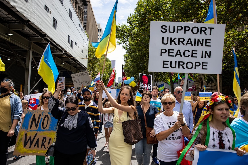 A crowd of demonstrators hold Ukrainian flags and placards reading "no war".