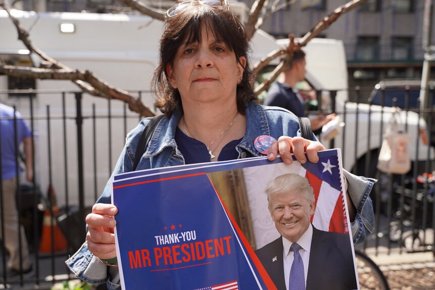 A woman wearing a denim jacket holds a sign saying THANK YOU MR PRESIDENT with Donald Trump's face on it