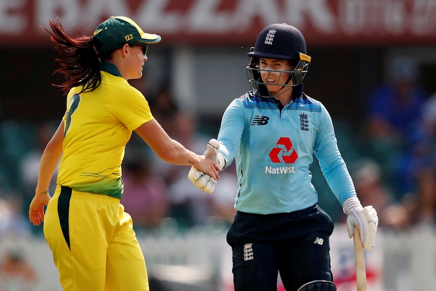 Megan Schutt, wearing yellow, shakes hands with Tammy Beaumont, wearing blue