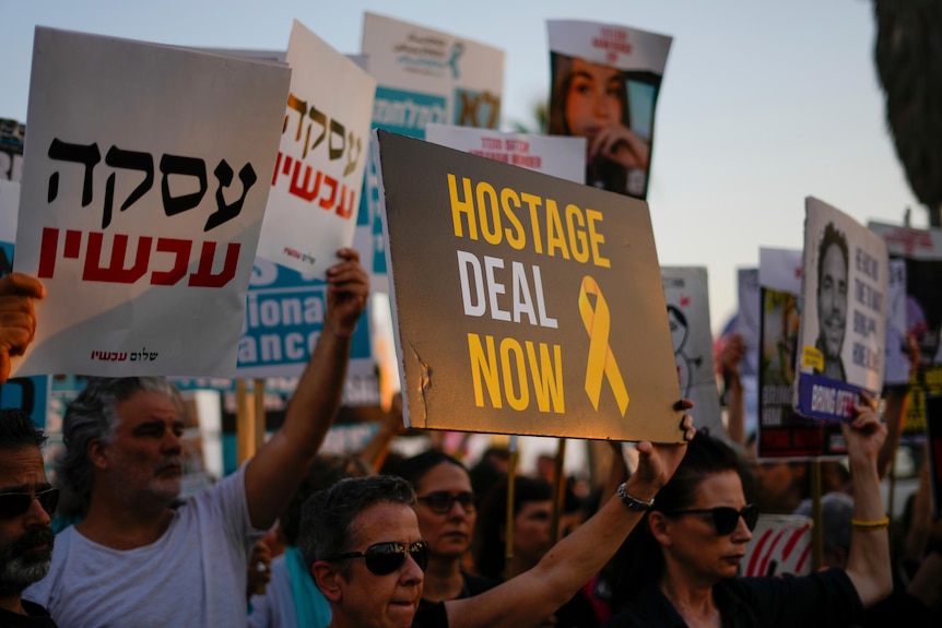 Protesters hold signs, including one that says "Hostage Deal Now" and others in foreign script. 