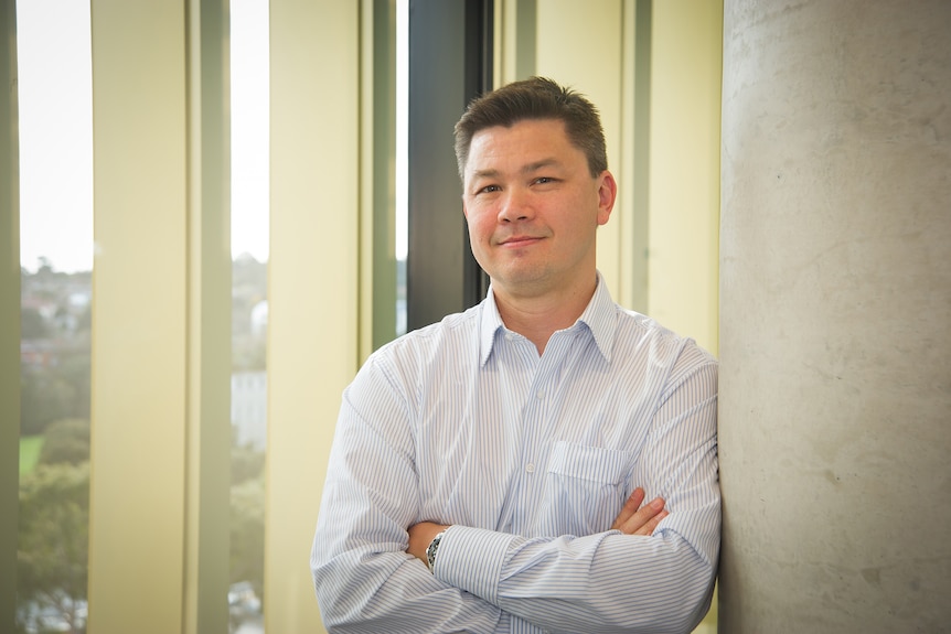 A man leans against a wall as he poses for a profile picture