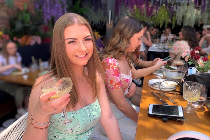 A girl holds a drink smiling at the camera. 