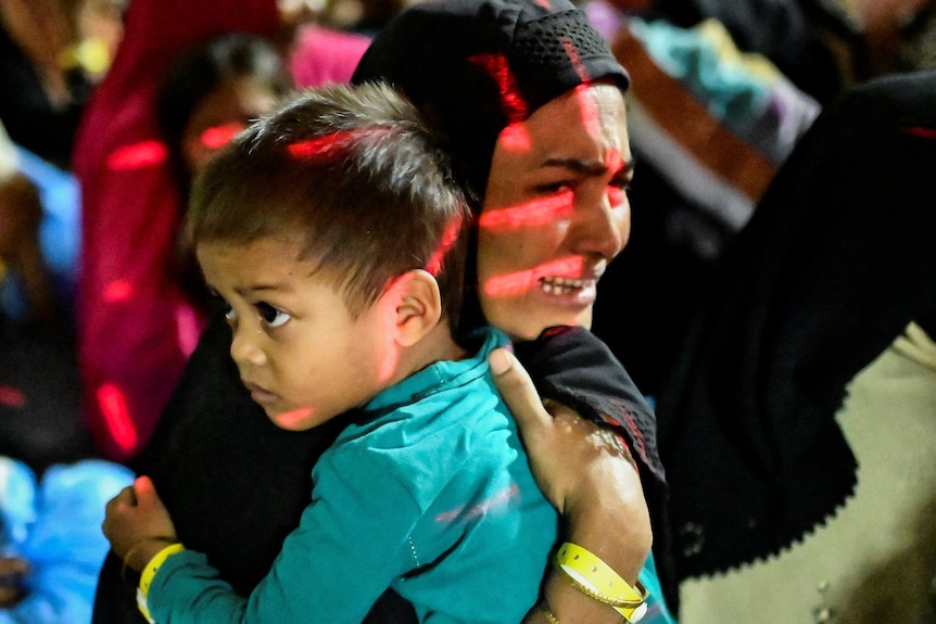 A Rohingya Muslim woman wearing hijab cries while holding her child close
