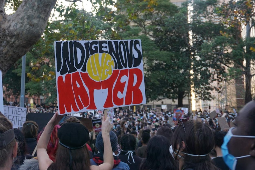 A person is holding a sign that says Indigenous lives matter at a protest in Sydney.