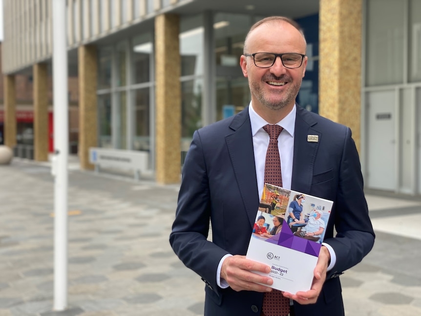Andrew Barr holding a copy of the ACT budget, while smiling.