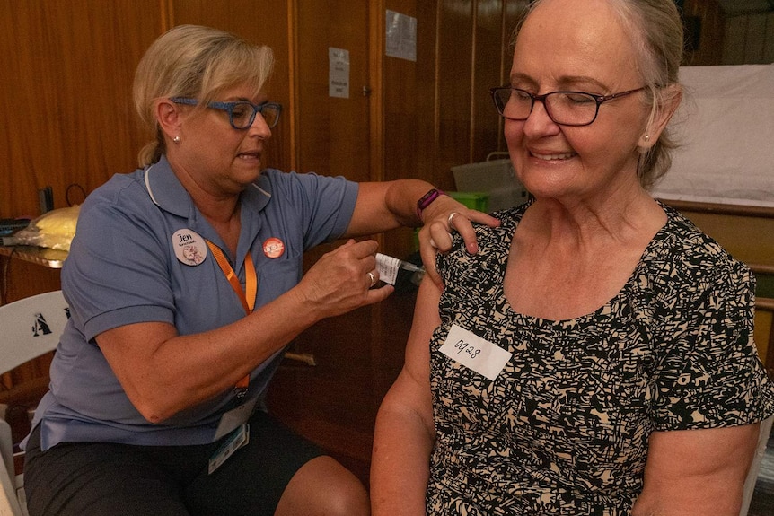 A nurse vaccinates a lady with her eyes closed and a smile on her face