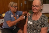A nurse vaccinates a lady with her eyes closed and a smile on her face