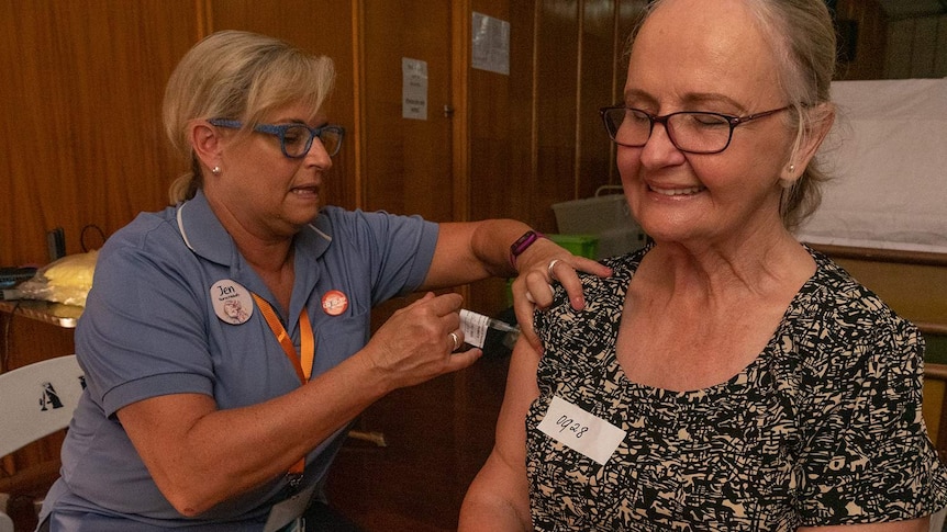 A nurse vaccinates a lady with her eyes closed and a smile on her face